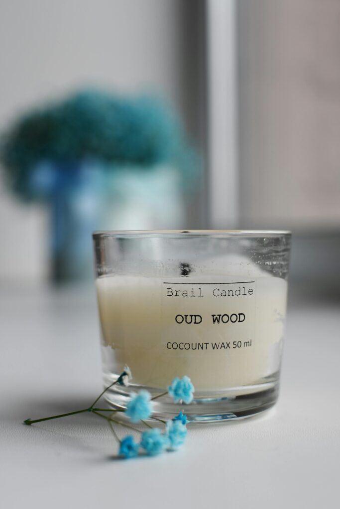 Still life of an Oud Wood candle, coconut wax in glass, with delicate blue flowers.