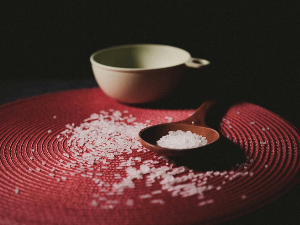 A wooden spoon with rice on a textured red mat, creating a warm, rustic feel.