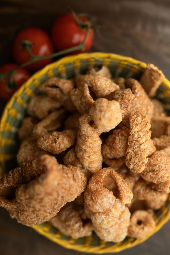 Close-up of crispy pork rinds in a basket with fresh tomatoes.