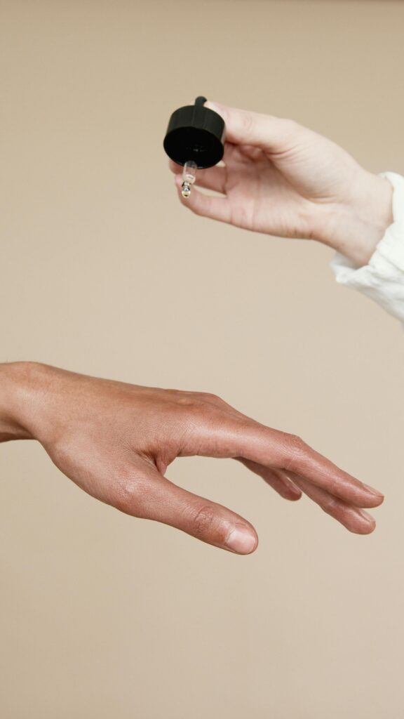 Two hands applying skin care oil with a dropper. Ideal for wellness and beauty themes.