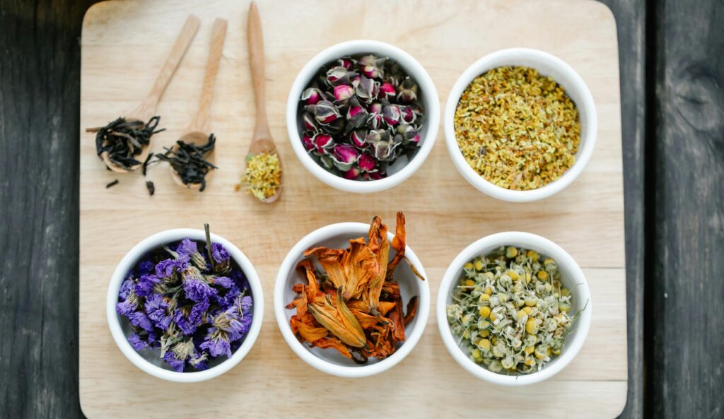 Colorful dried flowers and herbs displayed in bowls on a wooden board.