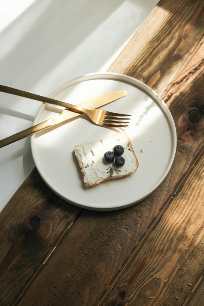 A minimalist plate with toast, cream cheese, and blueberries on a wooden table.