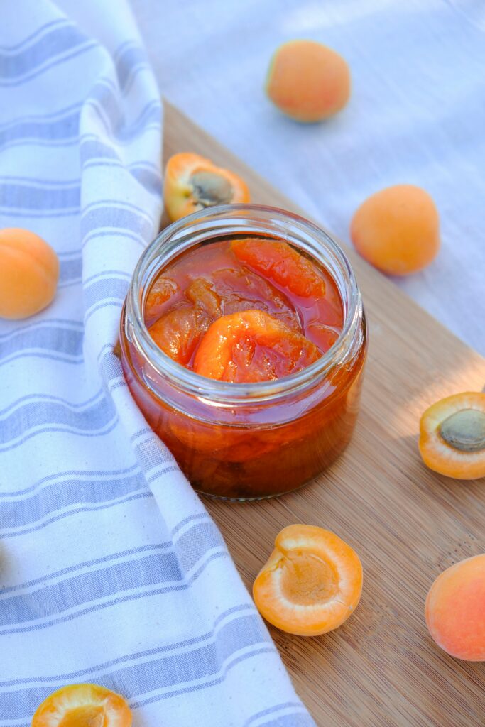 Delicious homemade peach jam in a glass jar on a wooden board, perfect for summer picnics.