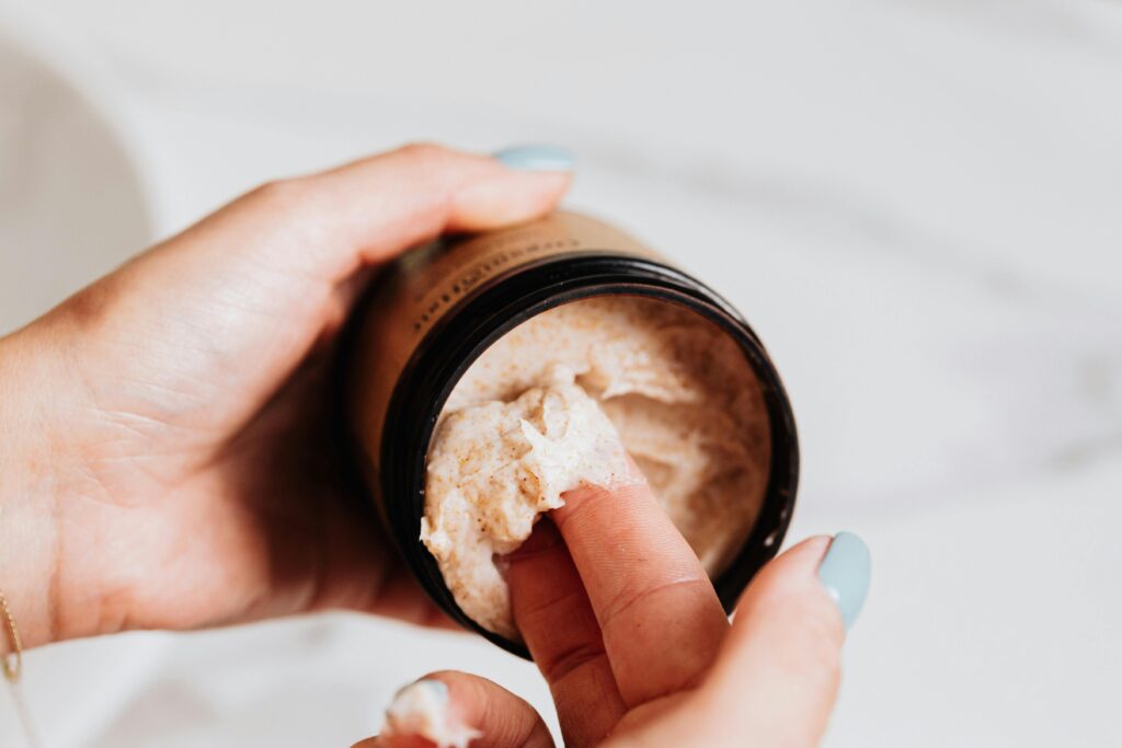 A hand applying skincare cream from a container, emphasizing self-care and beauty regimen.
