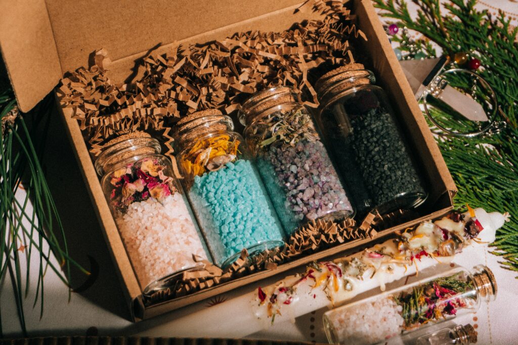 A diverse collection of colorful aromatic bath salts in glass jars packaged in a decorative gift box.