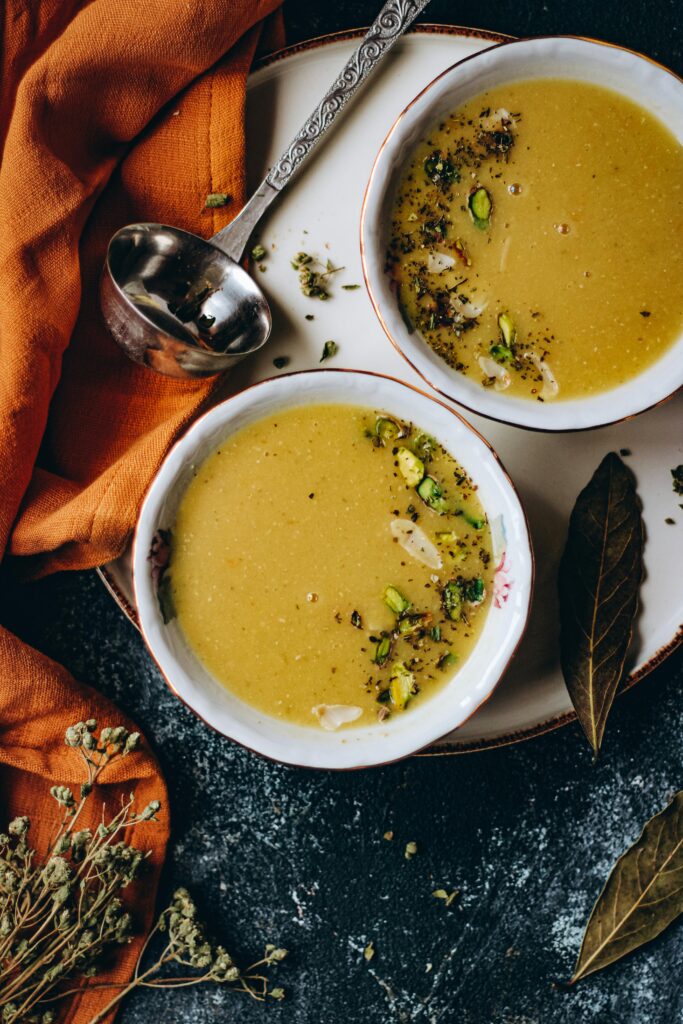 Top view of creamy soup garnished with herbs and pistachios, served in white bowls on a rustic surface.