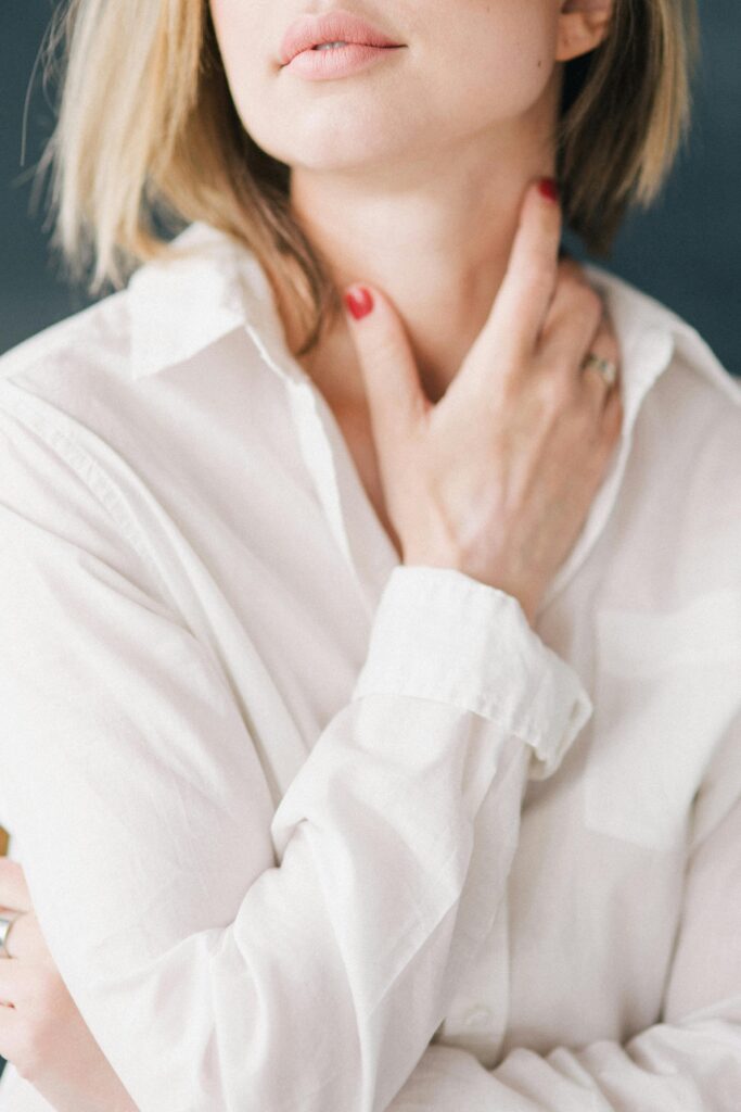 Close-up of a blonde woman with short hair, touching her neck, wearing a white shirt. Elegant and minimalist style.