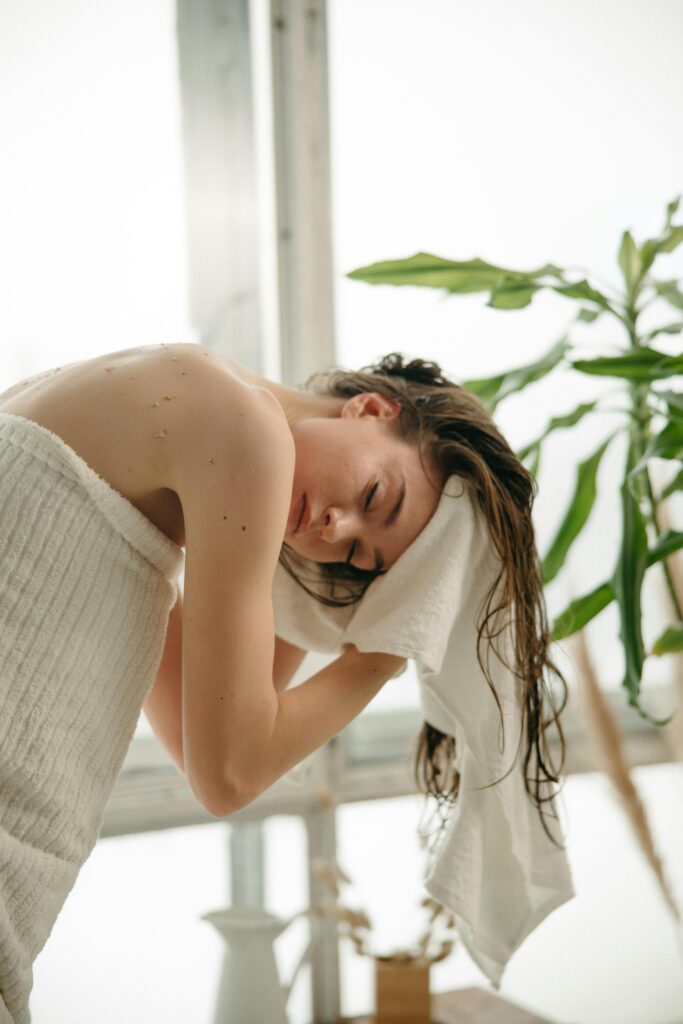 Relaxed woman drying her hair with a towel indoors, enjoying a moment of self-care.