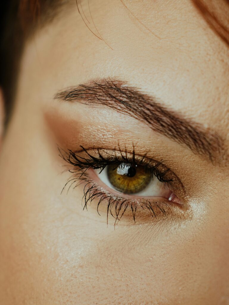 Detailed close-up of a woman's green eye with makeup, showcasing eyelashes and brow.